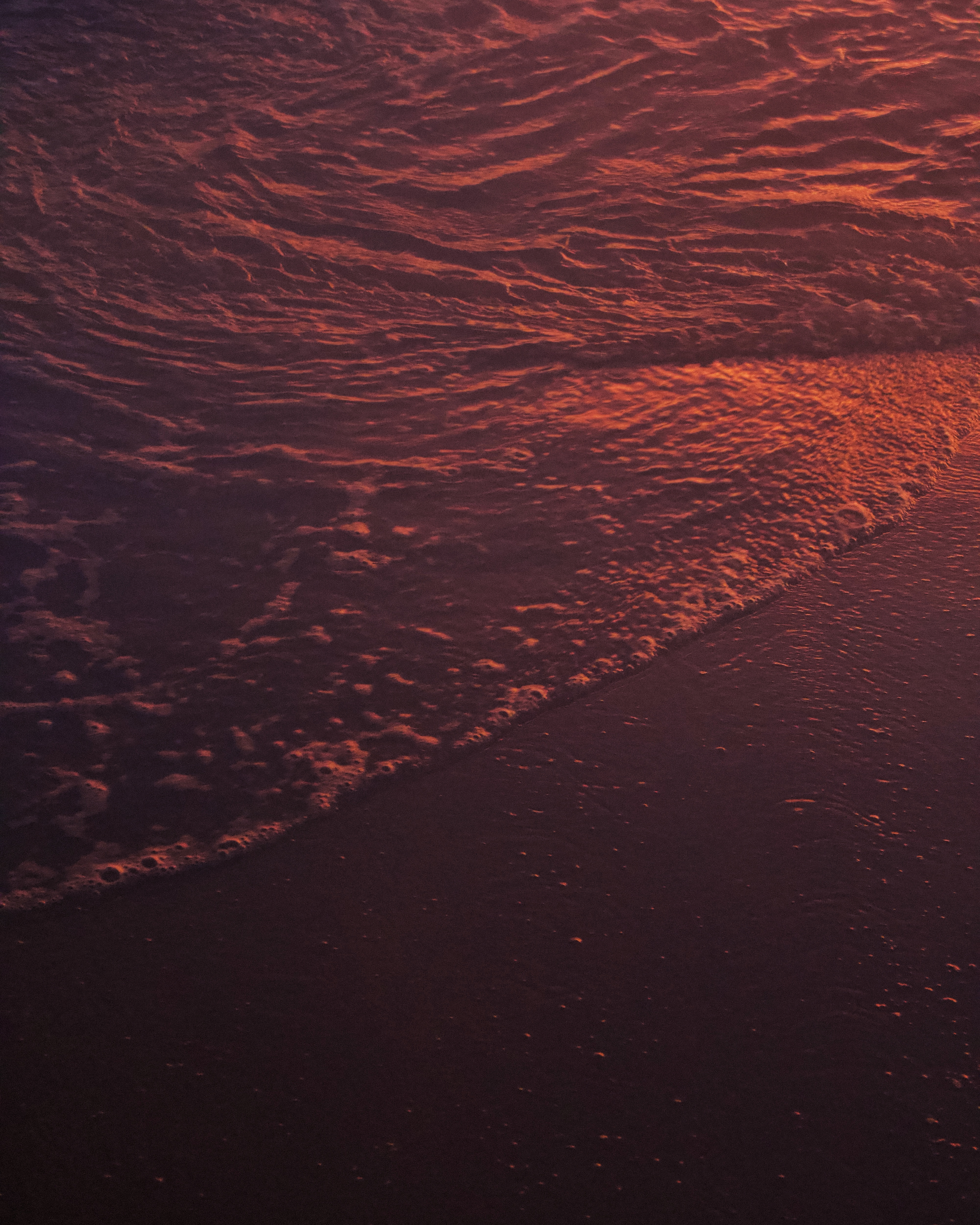 A dark wave breaking on sand at dusk